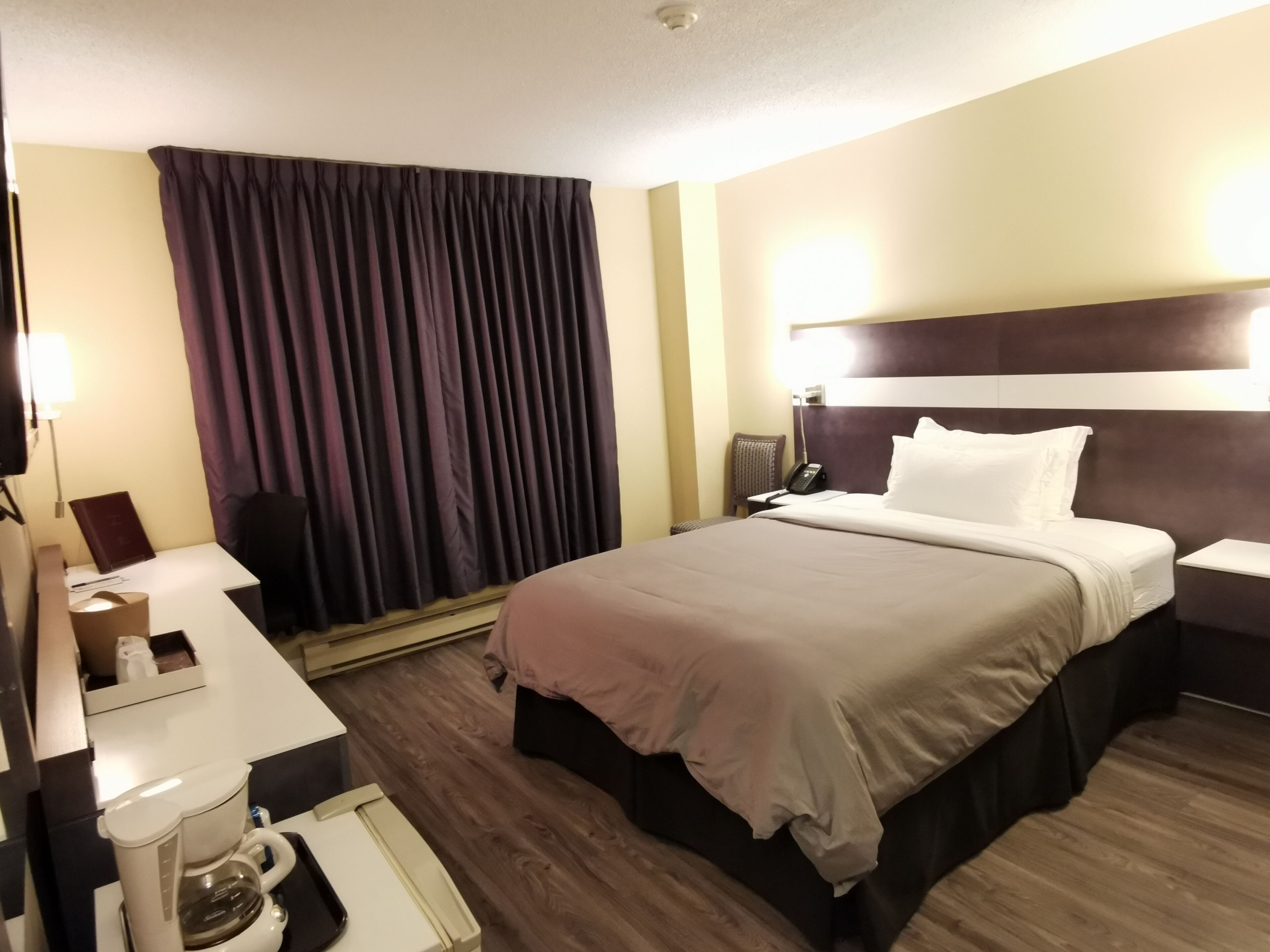 A hotel room with a bed, bedside table, lamp, and a coffee maker.