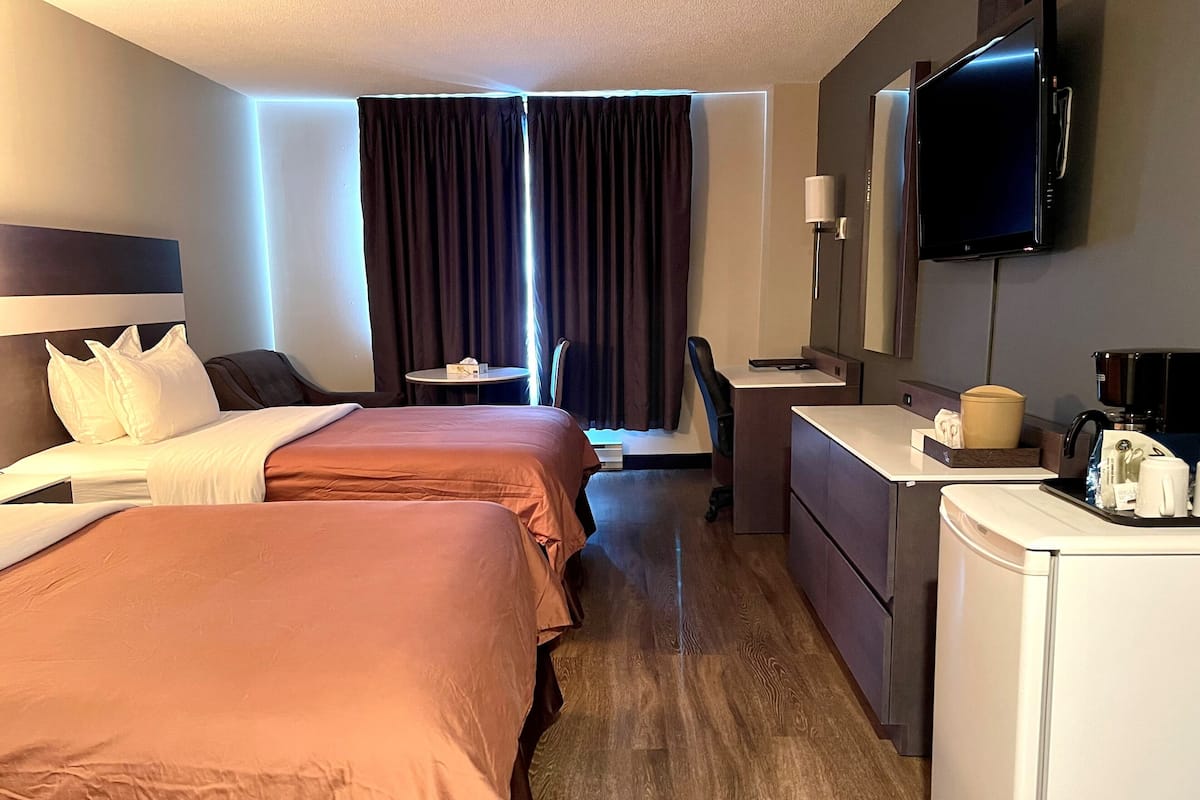 Habitación de hotel con dos camas, un escritorio, una silla, un televisor y una cafetera.