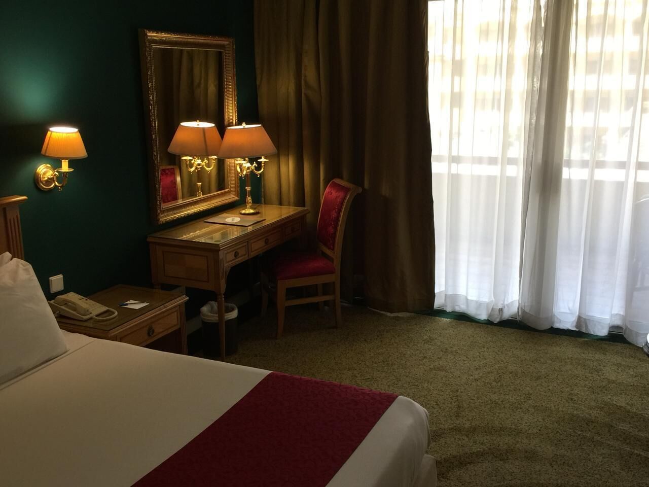 A hotel room with a bed, desk, chair, and a large mirror.