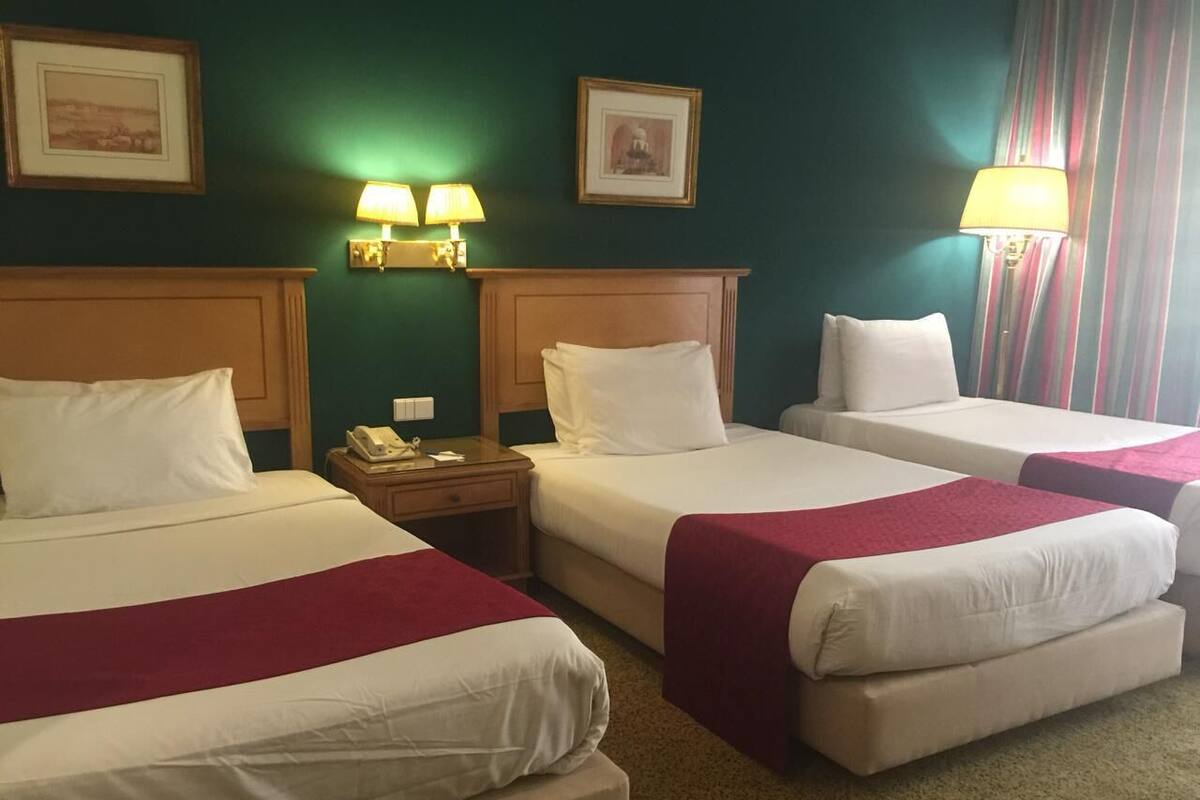 A hotel room with three beds, each with white linens and red blankets. There are two wall-mounted lamps on either side of the room.