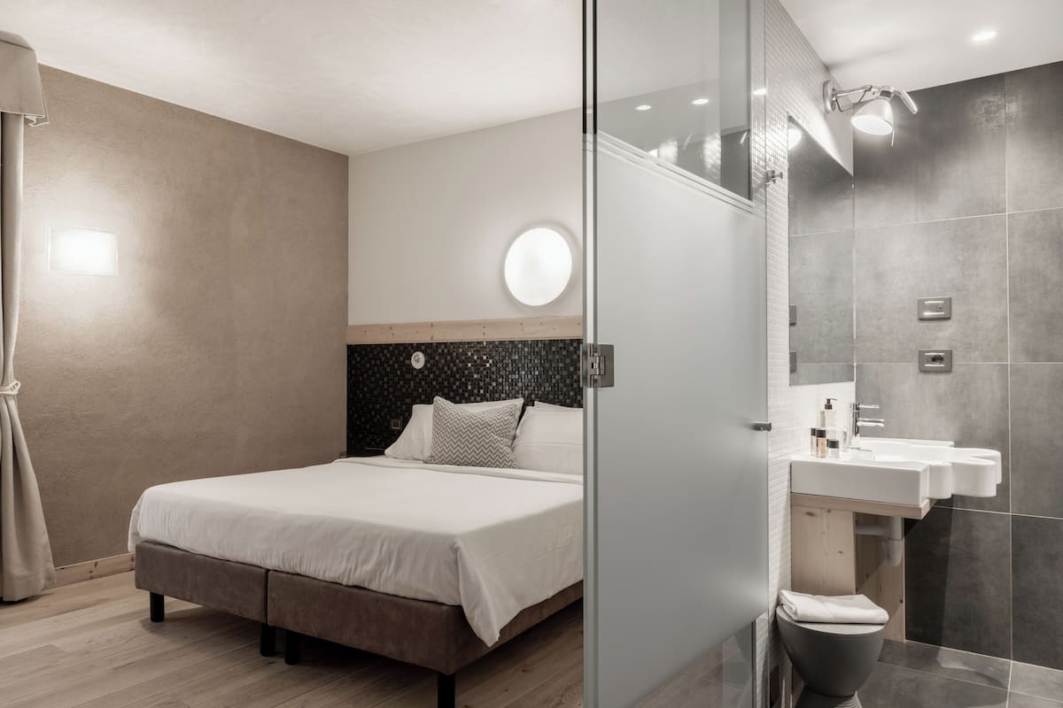 A modern bedroom with a bed, a round mirror, a built-in sink, and a toilet.