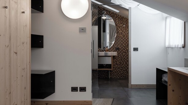 A modern bathroom with a large mirror, a round light fixture, and a tiled backsplash. - Hotel Orso Grigio (Cavalese)