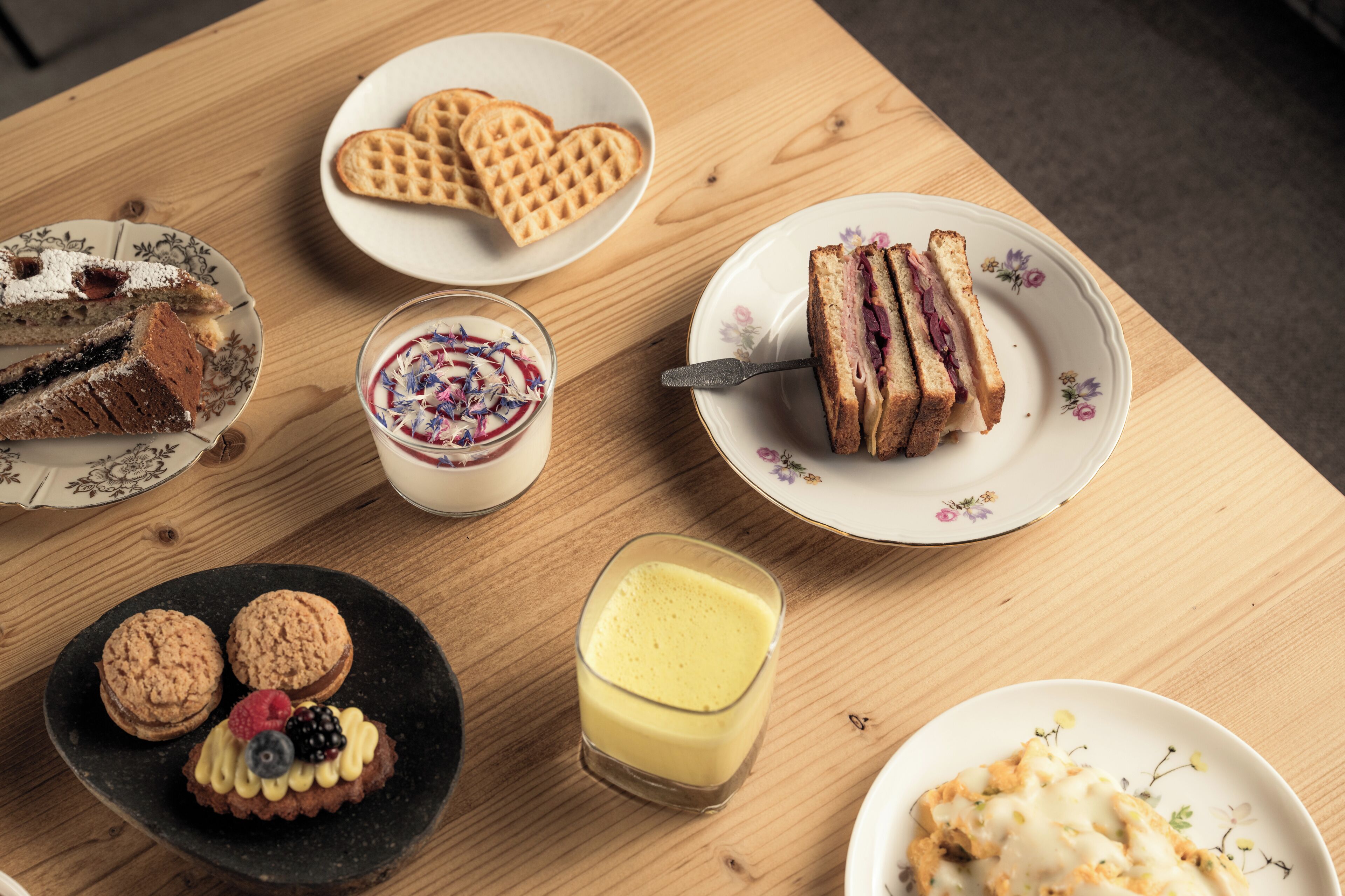 A wooden table with various desserts including a cake, waffles, and a glass of a yellow beverage.