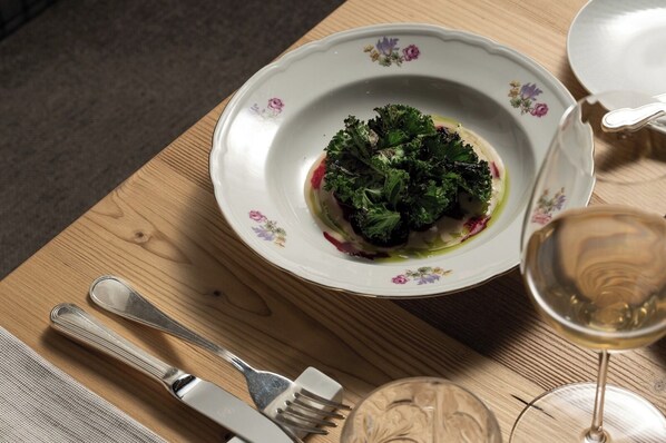 A dining table with a plate of food, a glass of wine, cutlery, and a decorative plate. - Hotel Orso Grigio (Cavalese)