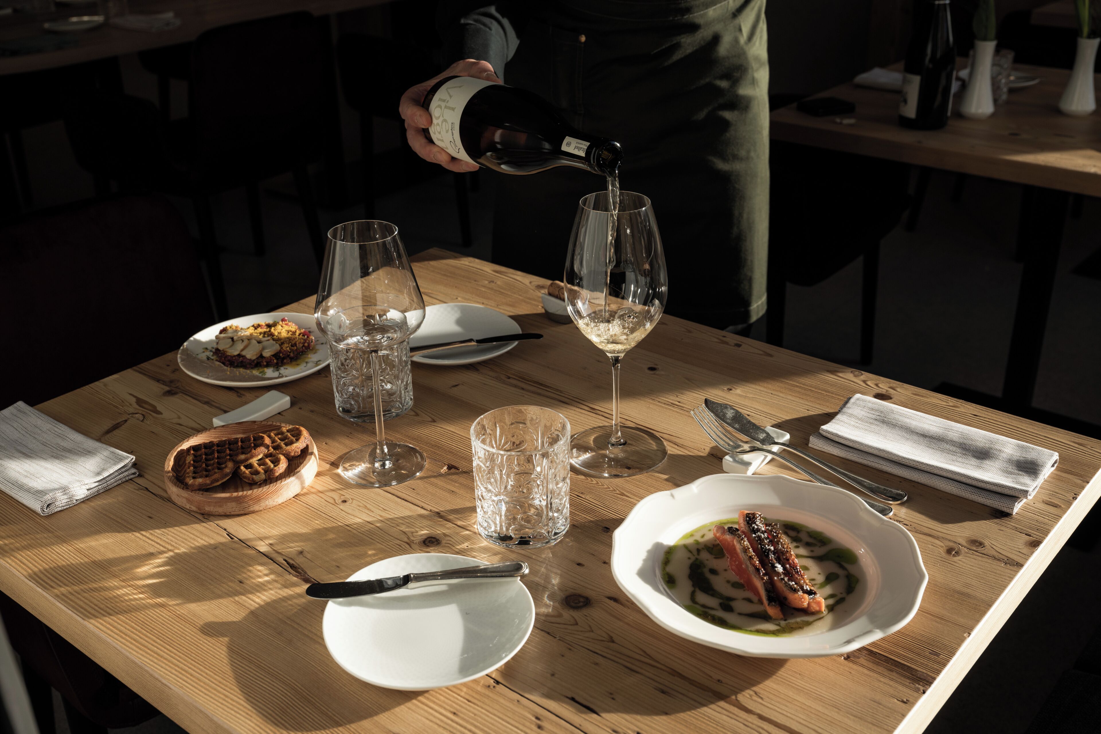 Un tavolo da pranzo con piatti di cibo, bicchieri da vino e una bottiglia che viene versata in un bicchiere.