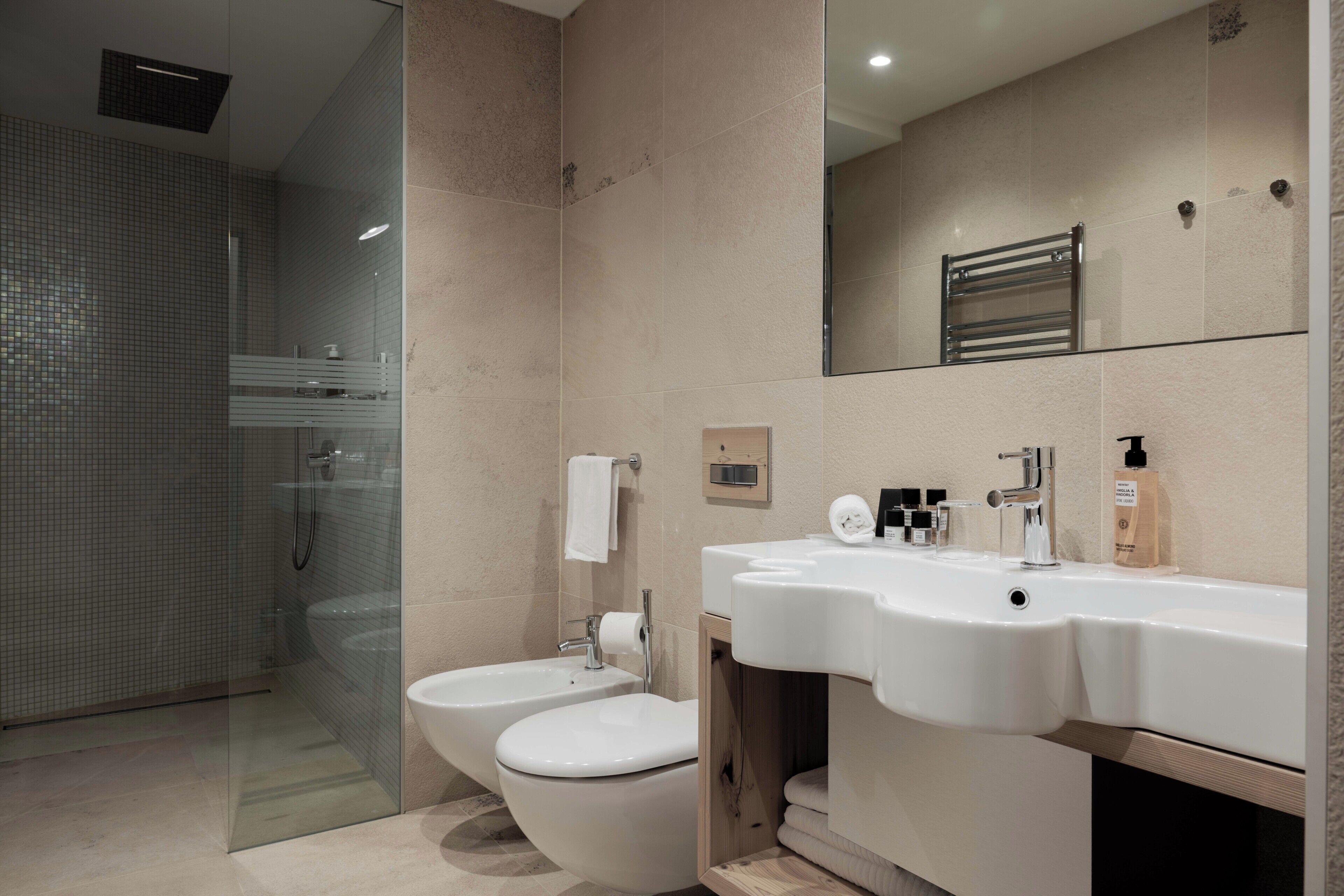 Une salle de bain moderne avec une douche à parois de verre, deux toilettes, un lavabo et un miroir.