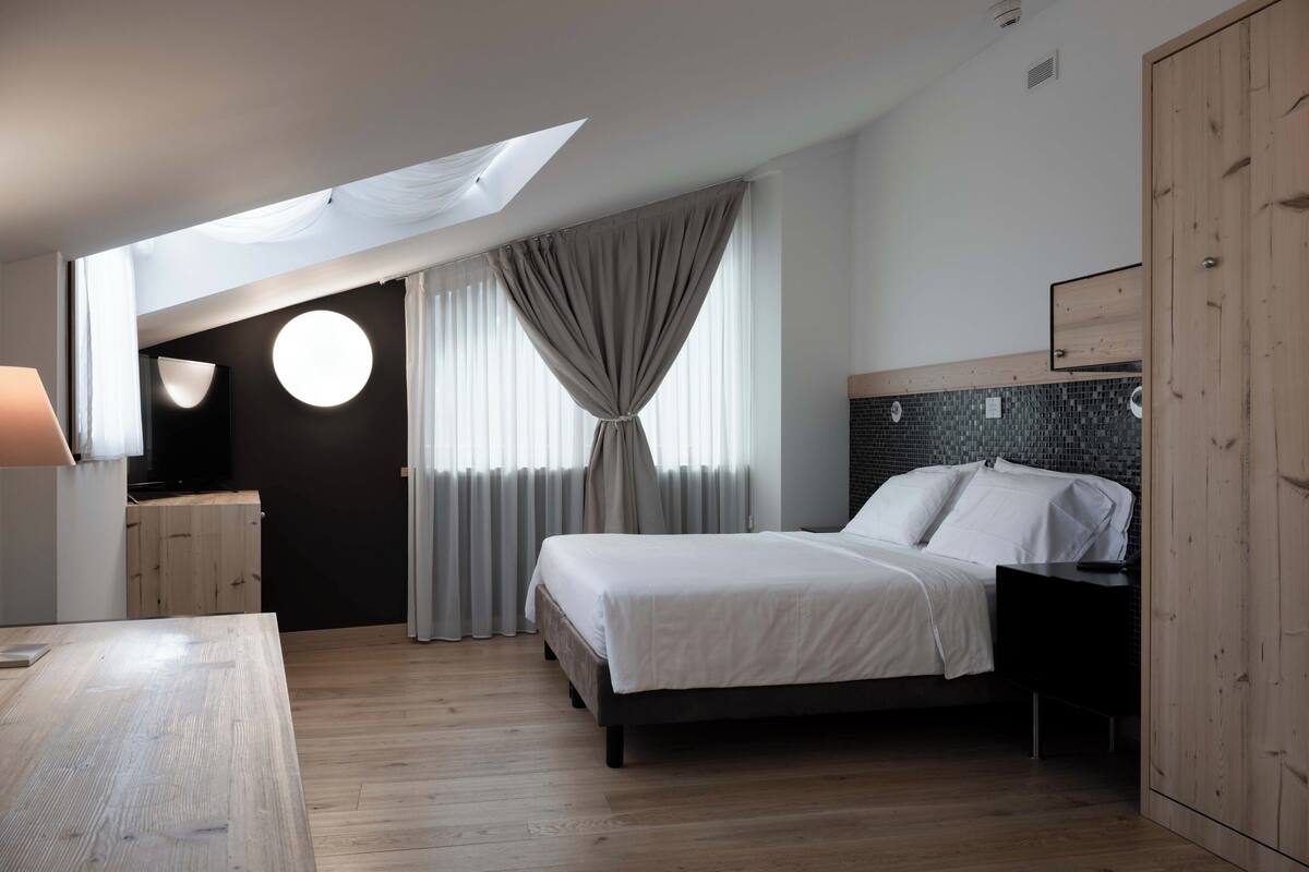 A modern bedroom with a skylight, a bed with white linens, a wooden desk, and a nightstand.