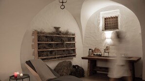 Una habitación con una silla de madera, una mesita con una lámpara y un ventanal de cuadrícula.