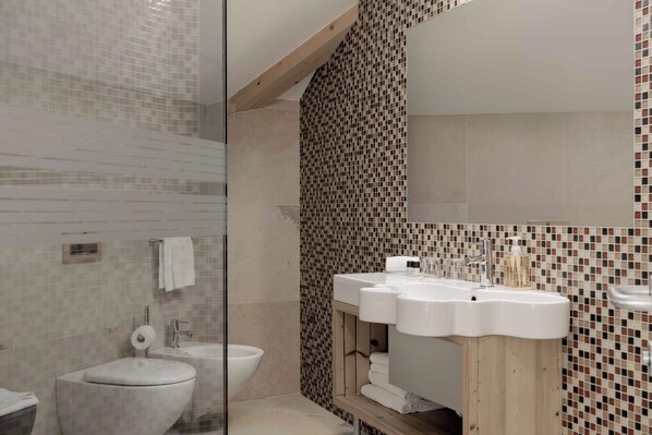A bathroom with a toilet, bidet, and a sink with a mirror. - Hotel Orso Grigio (Cavalese)