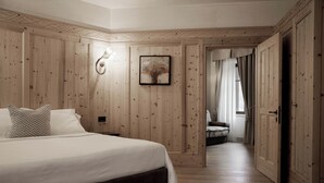 Un dormitorio con pared de paneles de madera, cama con ropa blanca, una obra de arte enmarcada y una puerta que da a otra habitación.