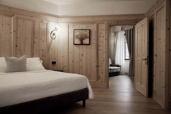A bedroom with a wooden paneled wall, a bed with white bedding, a framed artwork, and a door leading to another room. - Hotel Orso Grigio (Cavalese)