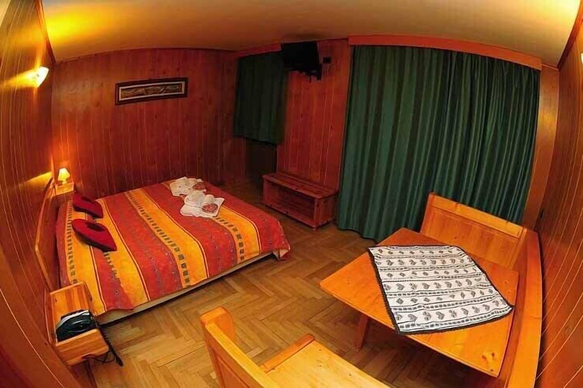 Una habitación de hotel compacta con cama, una mesita, una silla, un banco y una cortina.