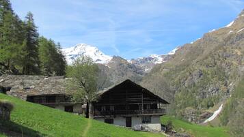 A traditional chalet with a sloped roof, set in a mountainous area with snow-capped peaks in the background.