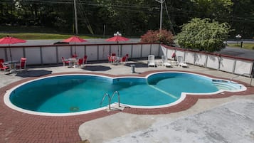 A swimming pool with a brick border, surrounded by red umbrellas and white chairs.