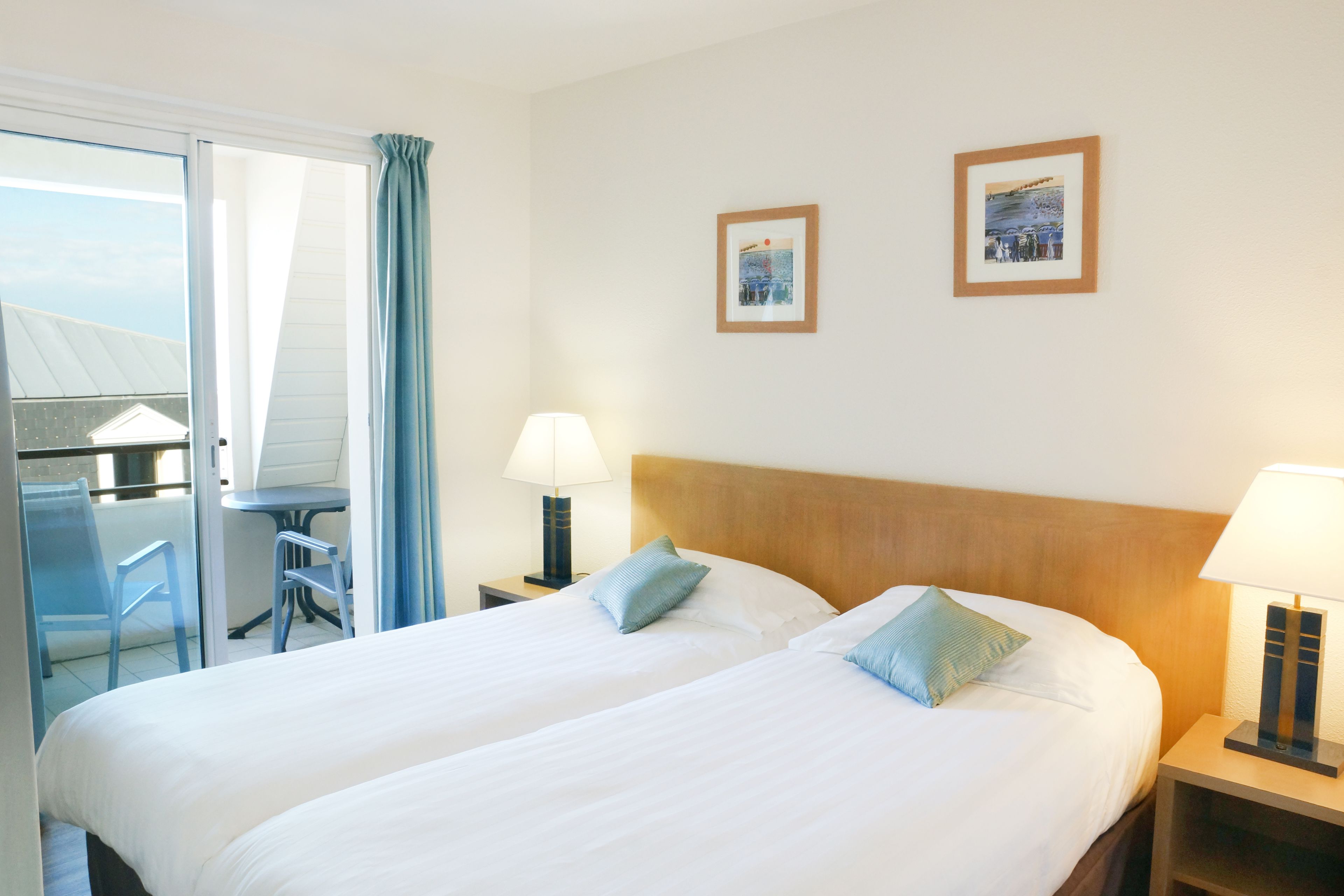 Habitación de hotel con dos camas, un balcón, una mesa y dos lámparas.