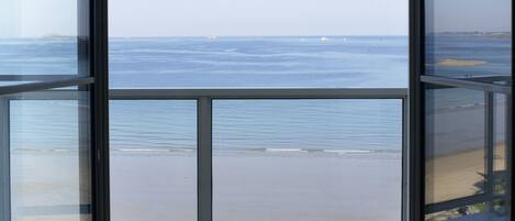 Vista a través de una ventana que muestra una playa, el océano y una isla distante.