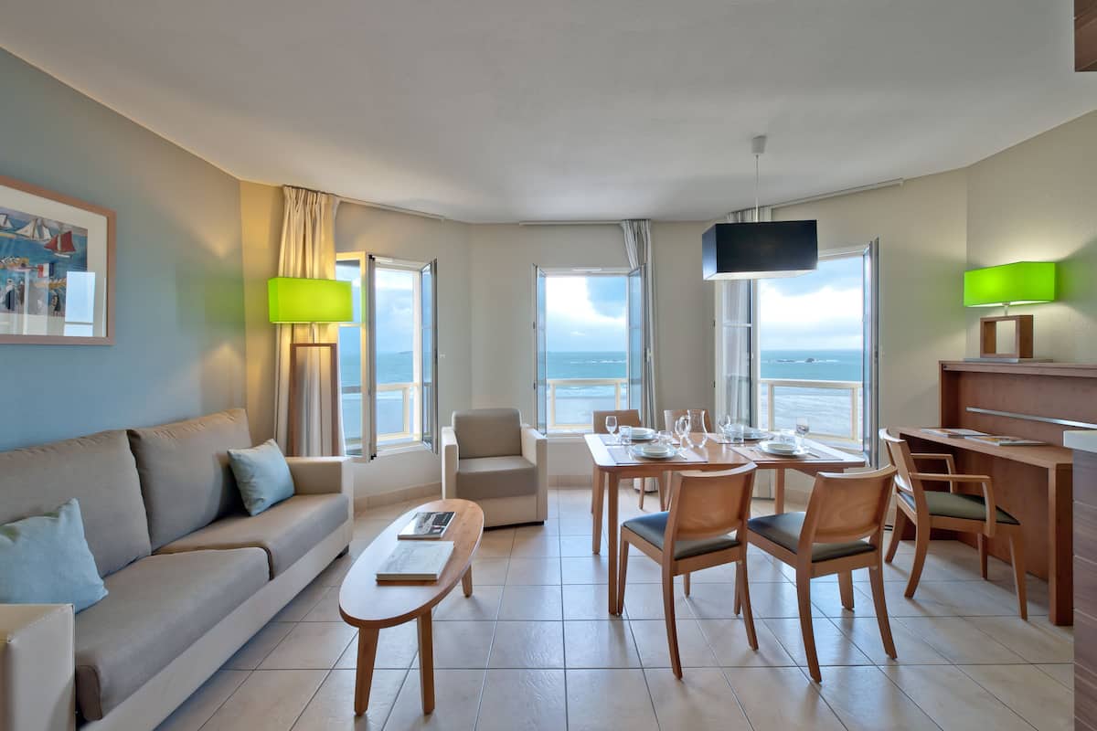 A modern hotel room with a balcony, a dining area, and a living space.