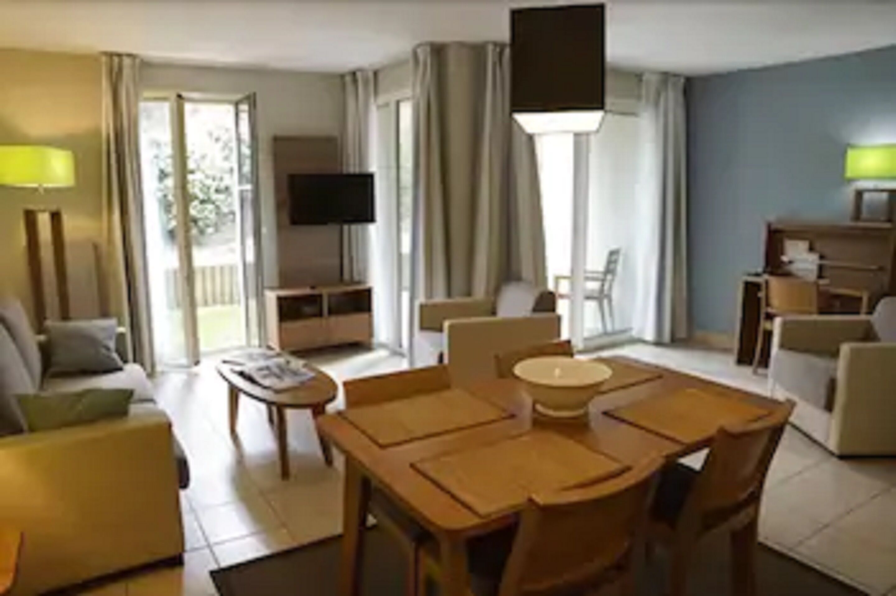 A hotel room with a dining area, a TV, and a balcony with curtains.