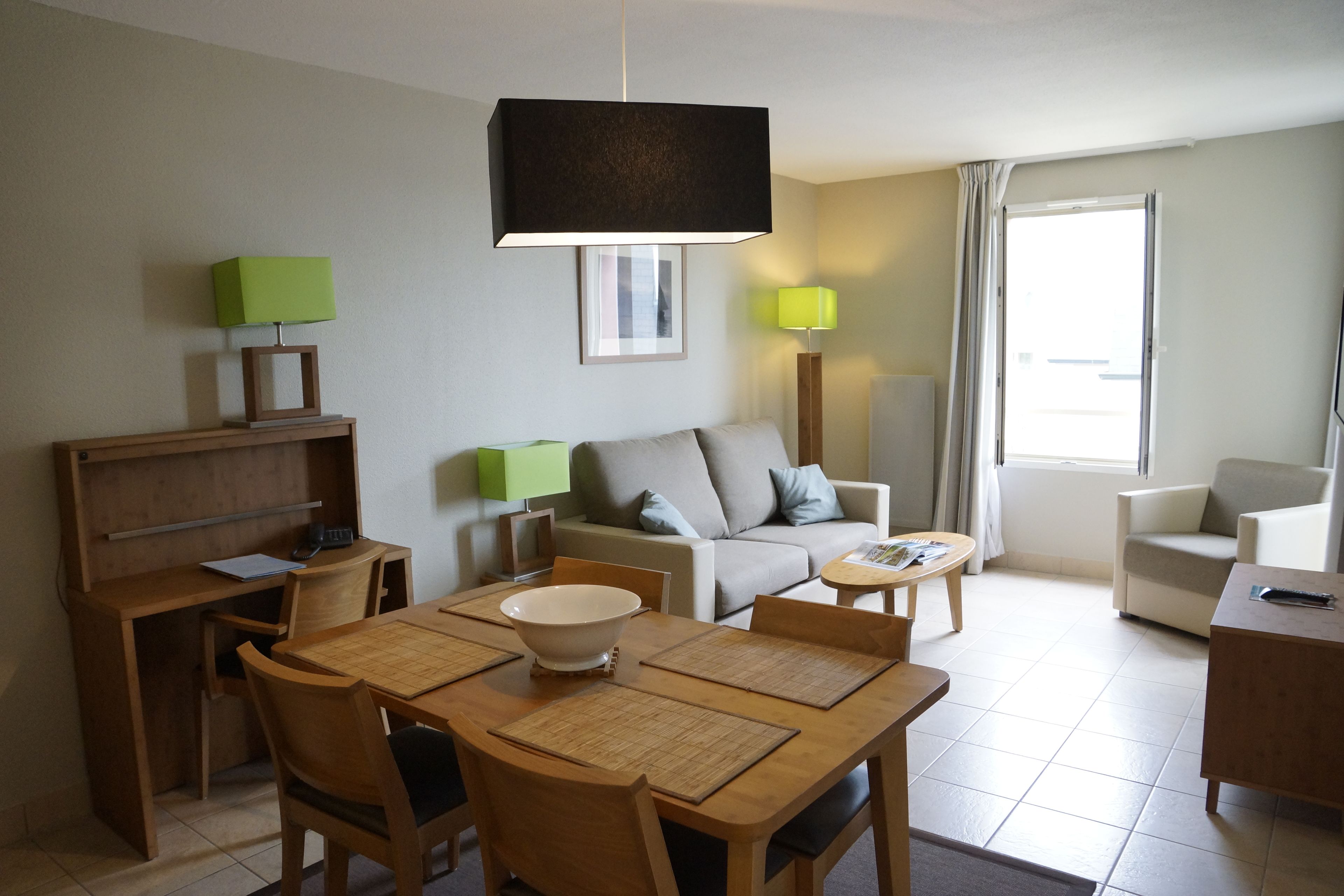 A modern living room with a dining area, featuring a wooden table, chairs, a sofa, and two lamps.