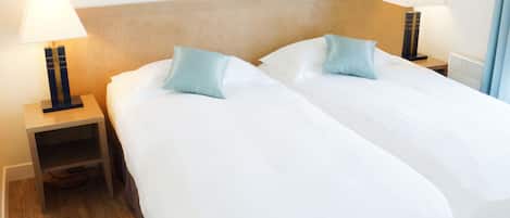 A hotel room with two beds, wooden headboard, bedside tables with lamps, and framed pictures on the wall.