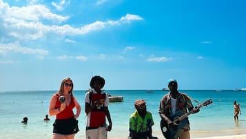 Escena de playa con gente, un guitarrista y una mesa con una bebida.