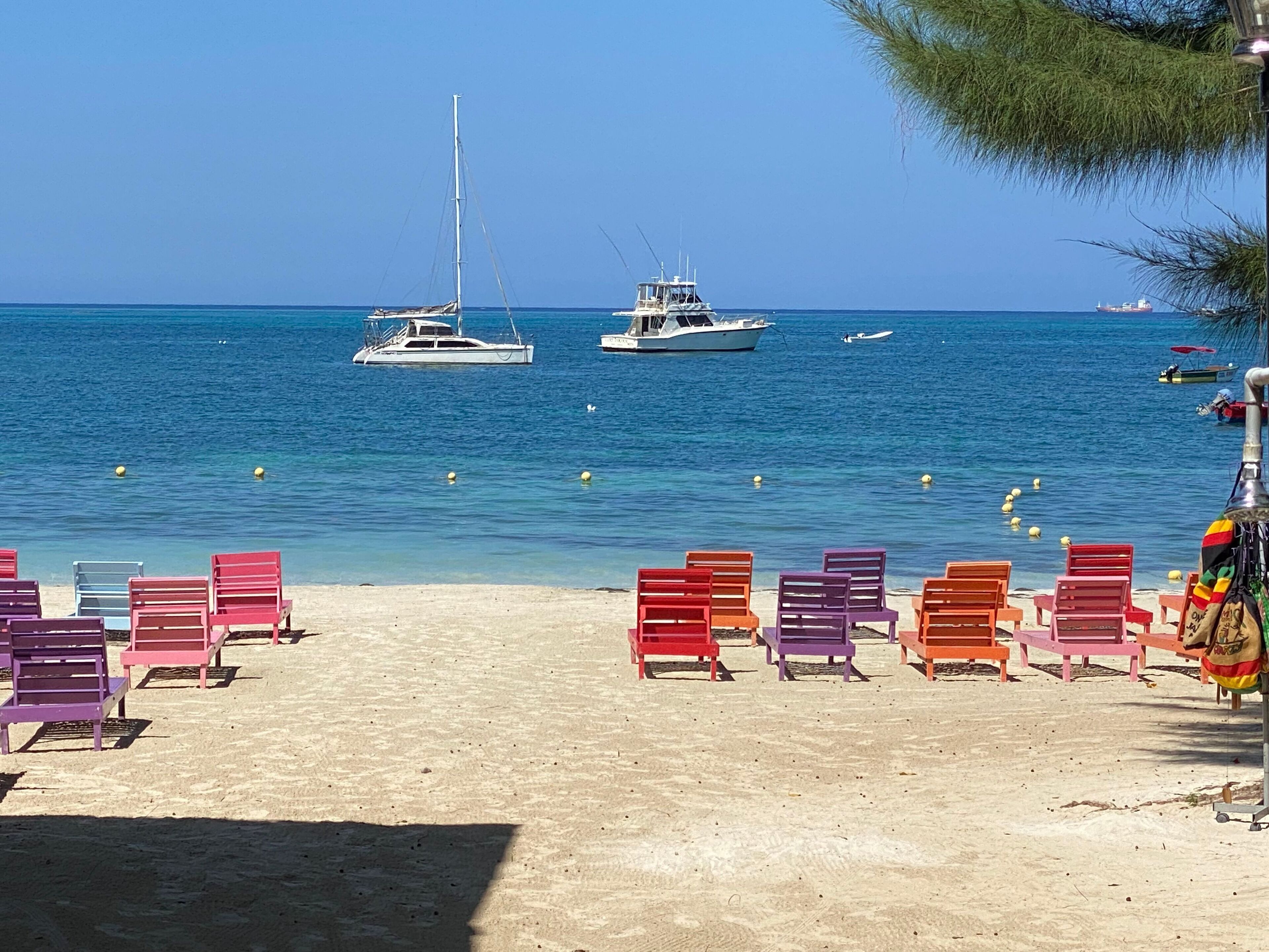 A beach with colorful lounge chairs and a clear view of the sea with boats.