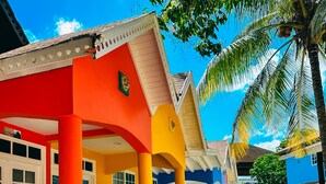 A colorful building with a porch, surrounded by plants and palm trees. - The Boardwalk Village (Negril)