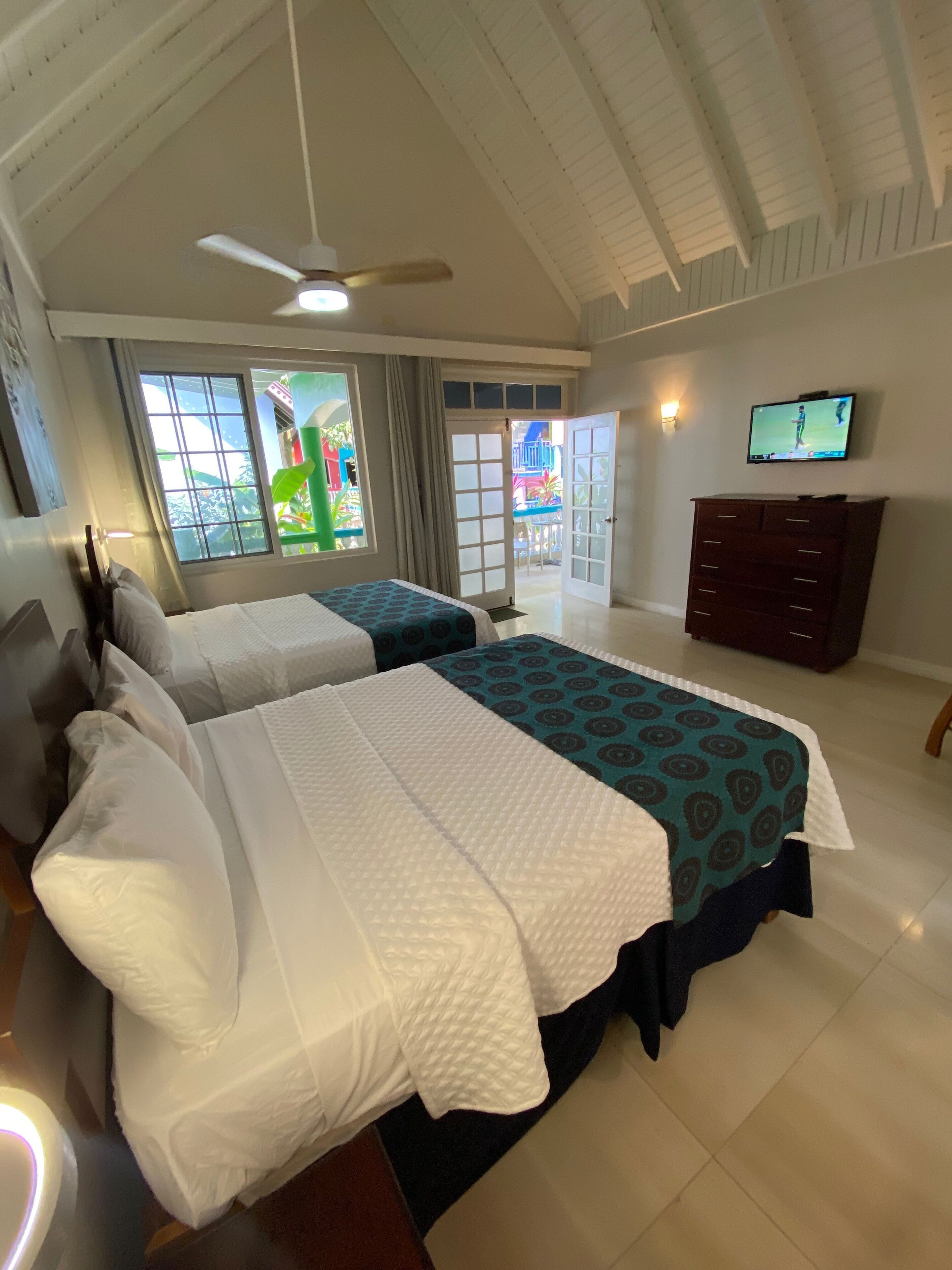 Une chambre d’hôtel avec deux lits, un ventilateur de plafond, une télévision et une vue sur l’extérieur.