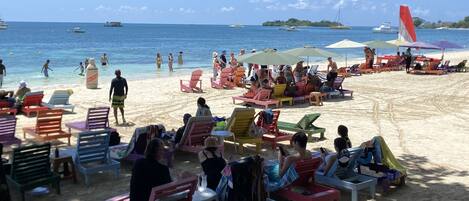 Una playa con sillas y sombrillas coloridas, una orilla arenosa y el océano al fondo.