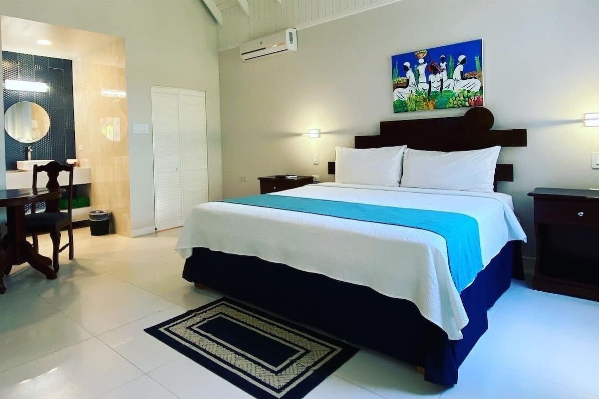A hotel room with a bed, bedside tables, a desk with a chair, a mirror, and a painting on the wall.