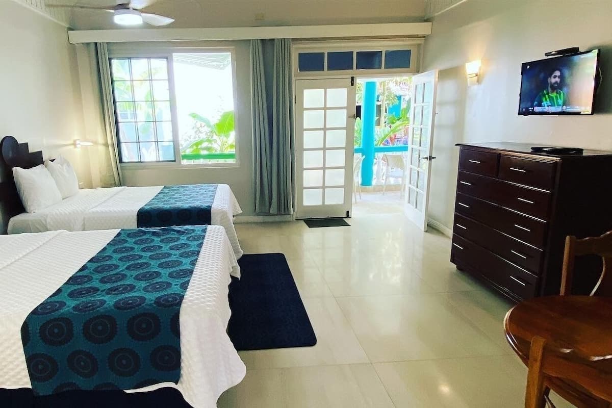 A hotel room with two beds, a TV, a dresser, and a view of the outside.