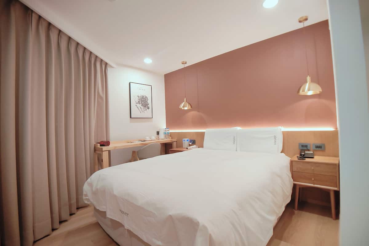 Ein modernes Hotelzimmer mit einem großen Bett, Nachttischen, einem Schreibtisch und einem Kopfteil mit integrierter Beleuchtung.