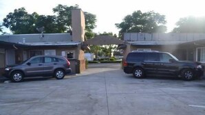 A parking lot with two cars parked in front of a building with a flat roof and a small entrance. - Searle Motel (Long Beach)