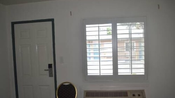 A room with a white door, a window with blinds, and a radiator. - Searle Motel (Long Beach)