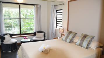 Ein Hotelzimmer mit einem großen Bett, zwei Sesseln, einem kleinen Tisch mit Blumenvase und einem Fenster mit Vorhängen.