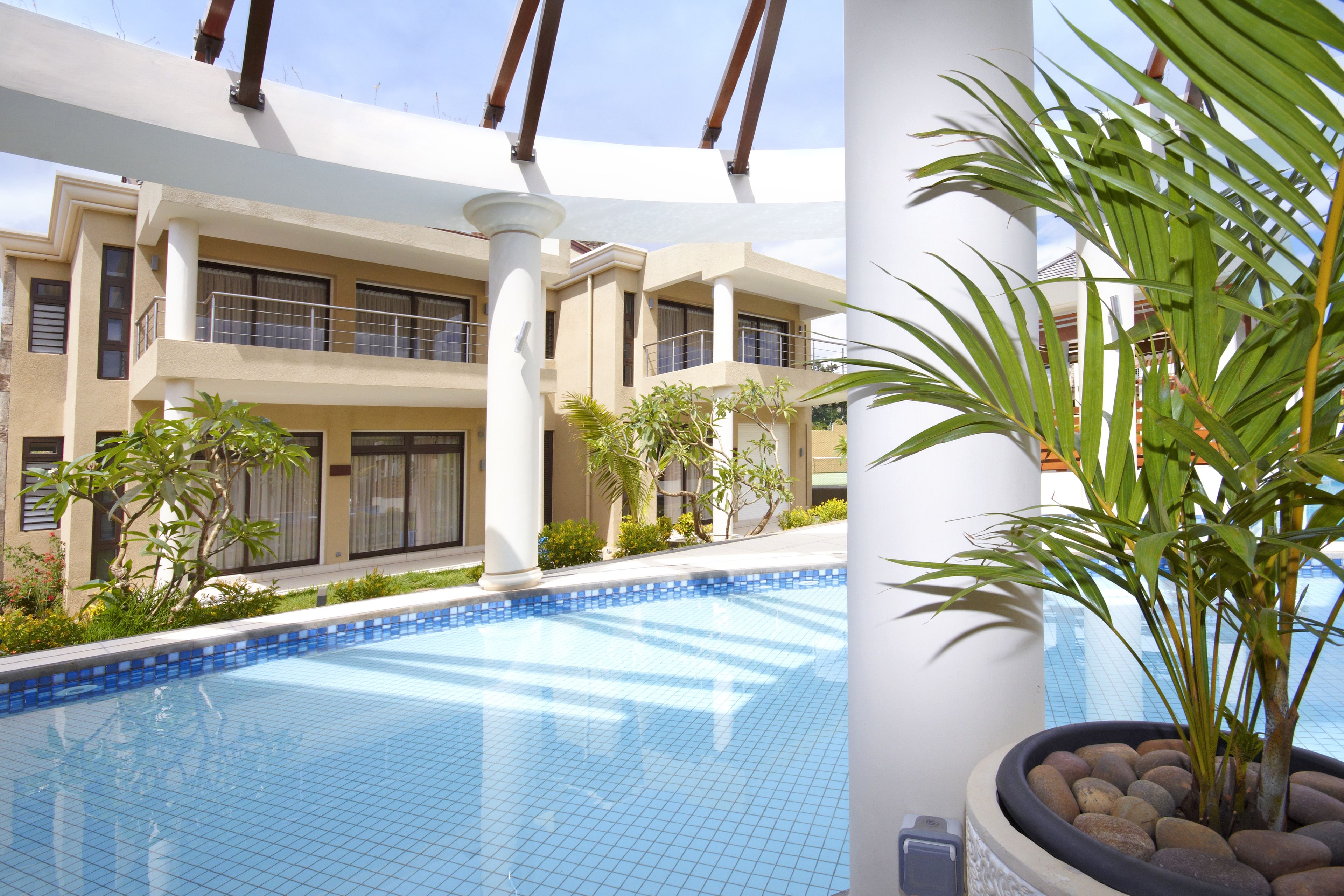 A pool area with tiled flooring, palm trees, and a building with multiple balconies and windows.