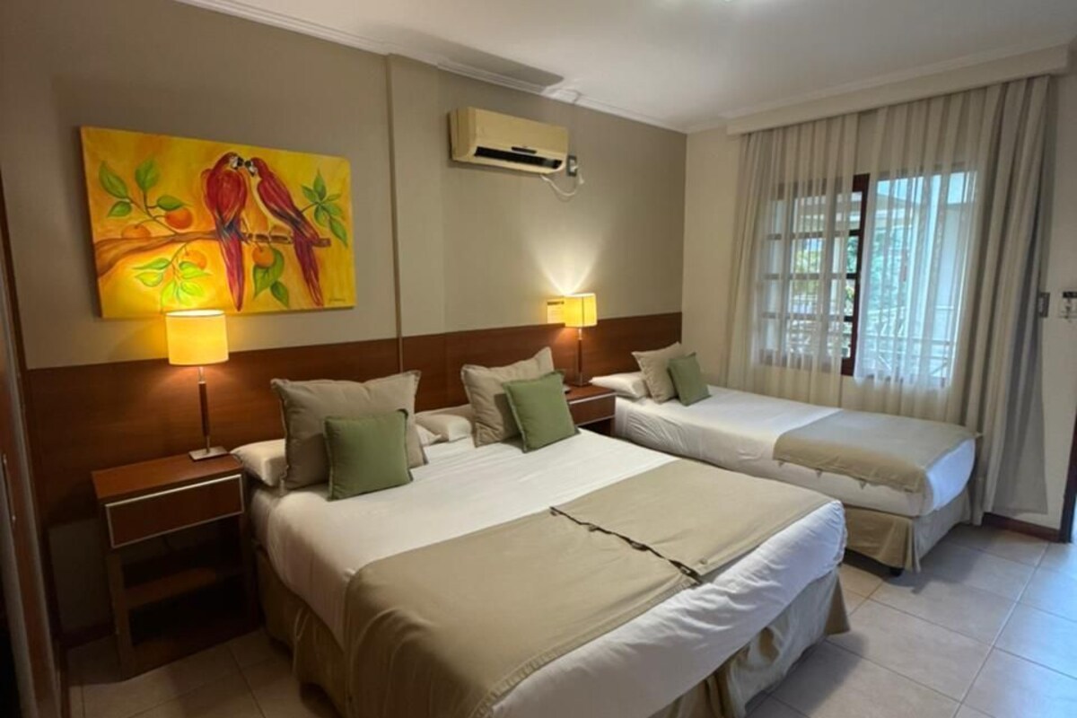 Una habitación de hotel con dos camas, un cuadro, un equipo de aire acondicionado, una mesita de noche y una ventana con cortinas.