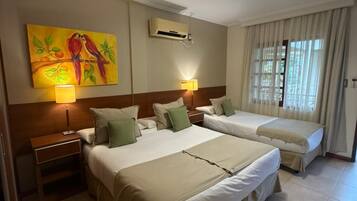 Una habitación de hotel con dos camas, un cuadro, un equipo de aire acondicionado, una mesita de noche y una ventana con cortinas.