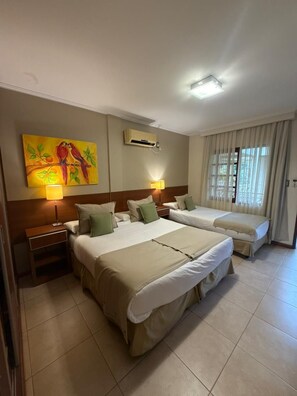 A hotel room with two beds, a painting, an air conditioning unit, a nightstand, and a window with curtains. - Hotel Jardin de Iguazu (Puerto Iguazú)