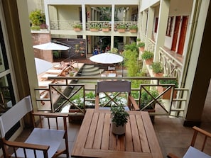 A balcony with wooden furniture, a potted plant, and a view of a courtyard with multiple levels and balconies. - Hotel Jardin de Iguazu (Puerto IguazĂș)