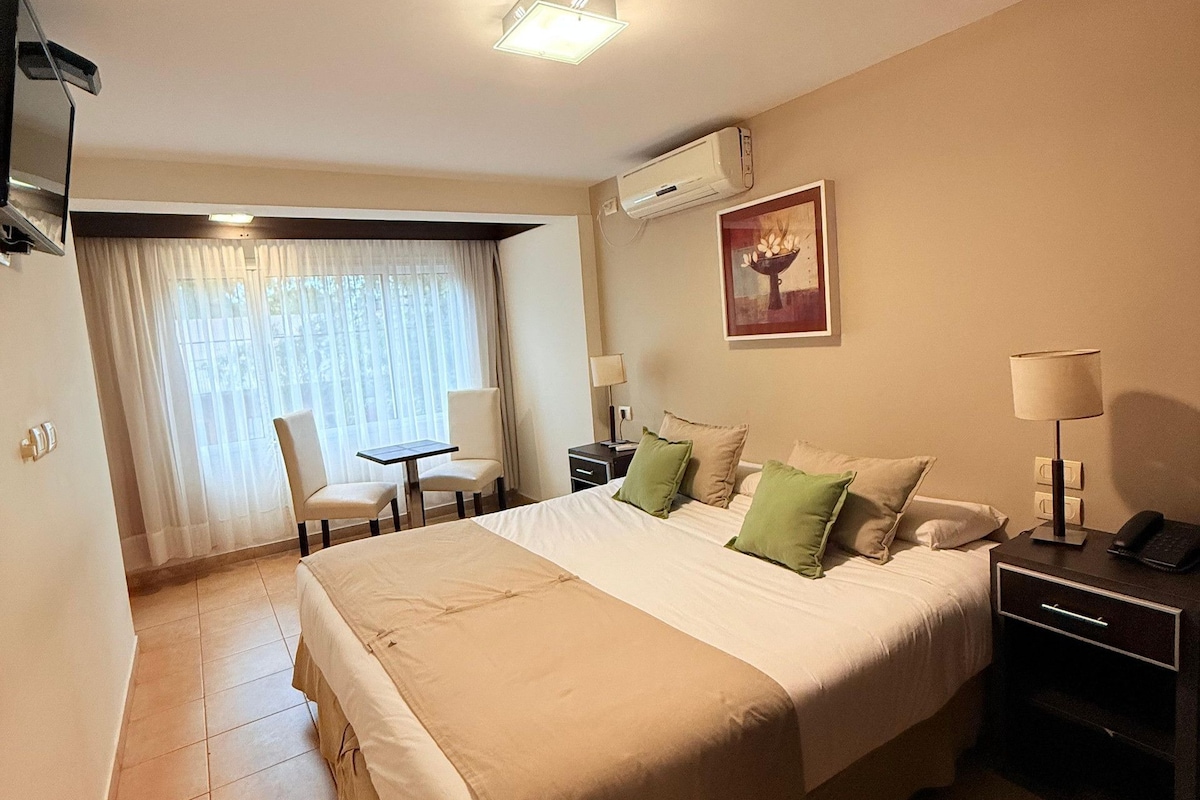 Una habitación de hotel con una cama grande, mesitas de noche, un escritorio y una silla.