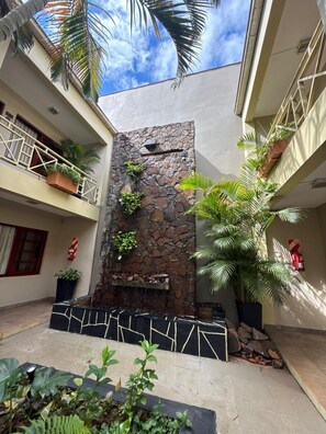 A courtyard with a stone wall, potted plants, and a fire extinguisher. - Hotel Jardin de Iguazu (Puerto Iguazú)