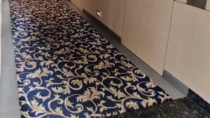 A hallway with patterned carpet, beige walls, and a tiled floor. - Landmark Residency (Mumbai)