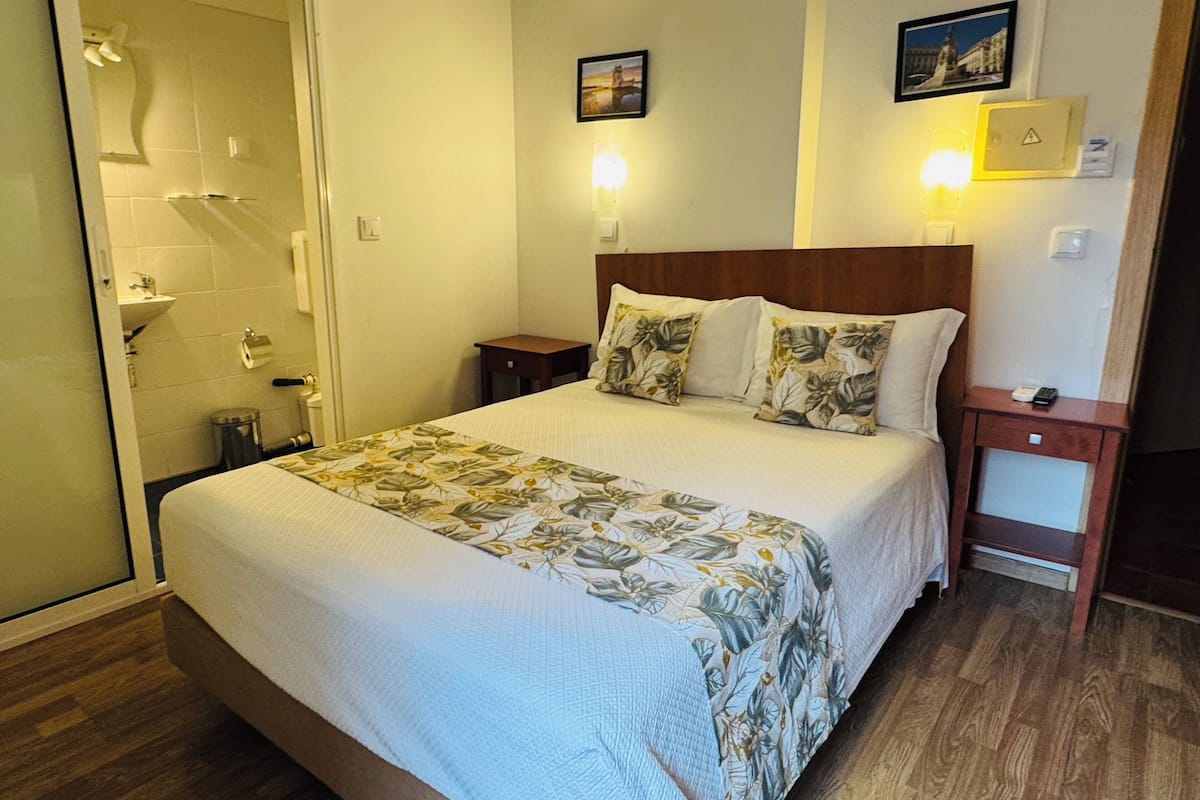 A hotel room with a bed, a nightstand, a bedside table, a lamp, and a picture on the wall.