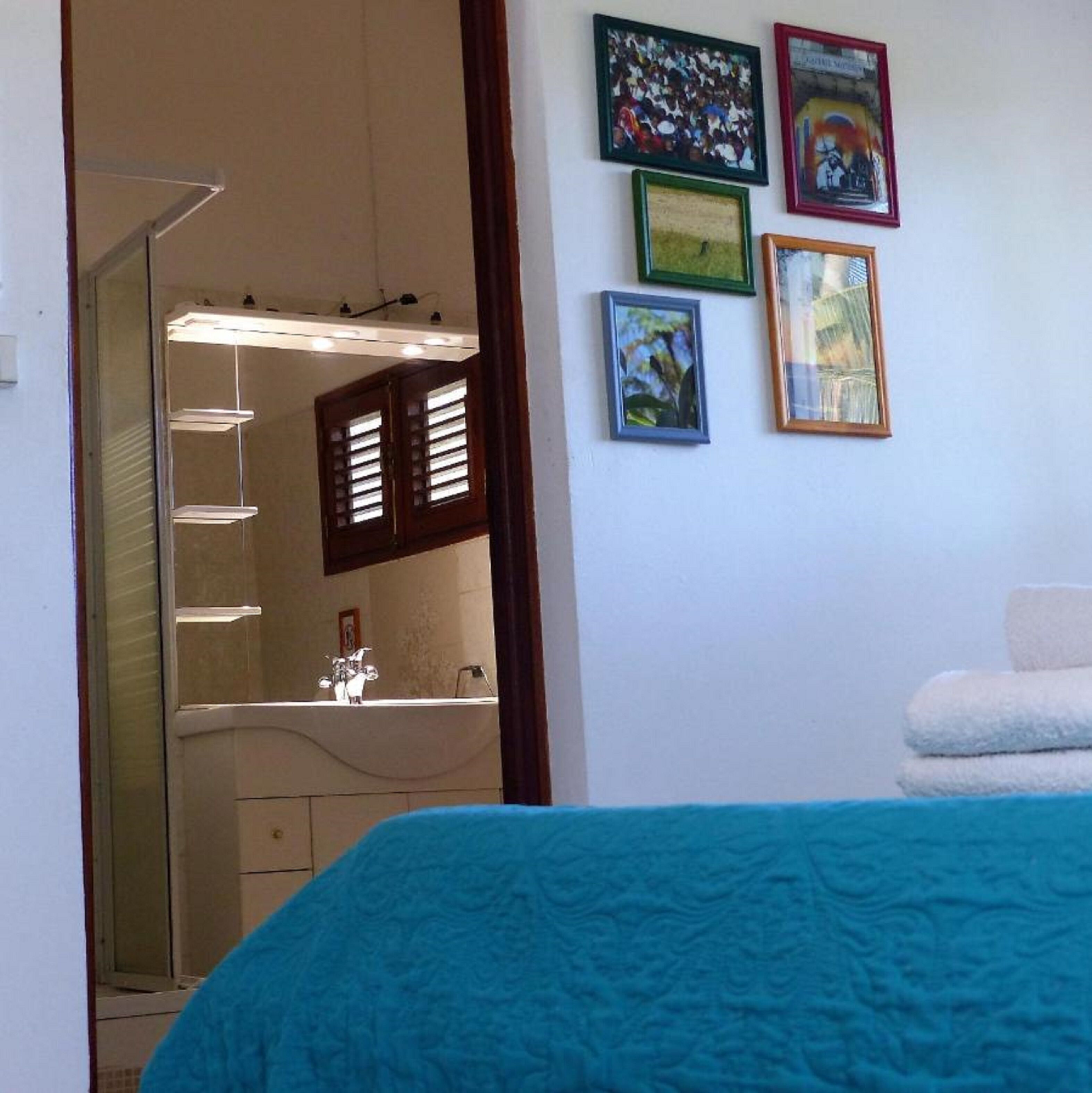 Une chambre avec un lit, une salle de bain avec un lavabo et un miroir. Il y a quatre tableaux encadrés accrochés au mur.