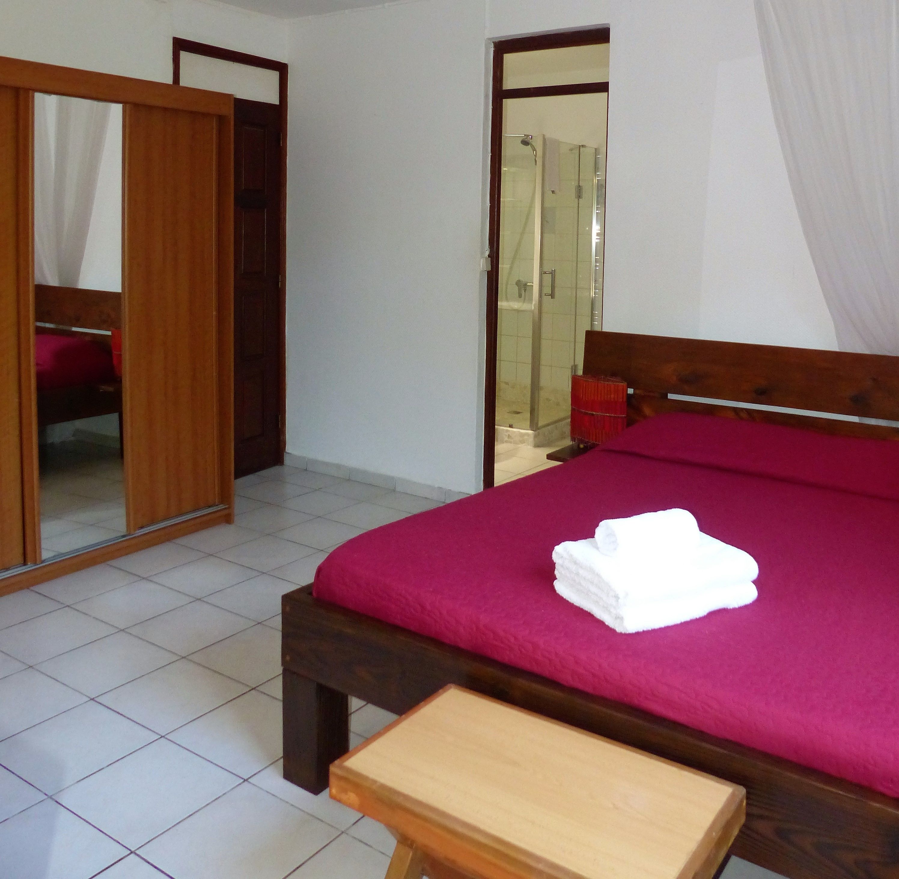 A bedroom with a bed, a wooden bench, a wardrobe, and a bathroom visible through an open door.