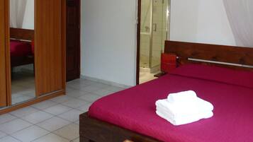 A bedroom with a bed, a wooden bench, a wardrobe, and a bathroom visible through an open door.