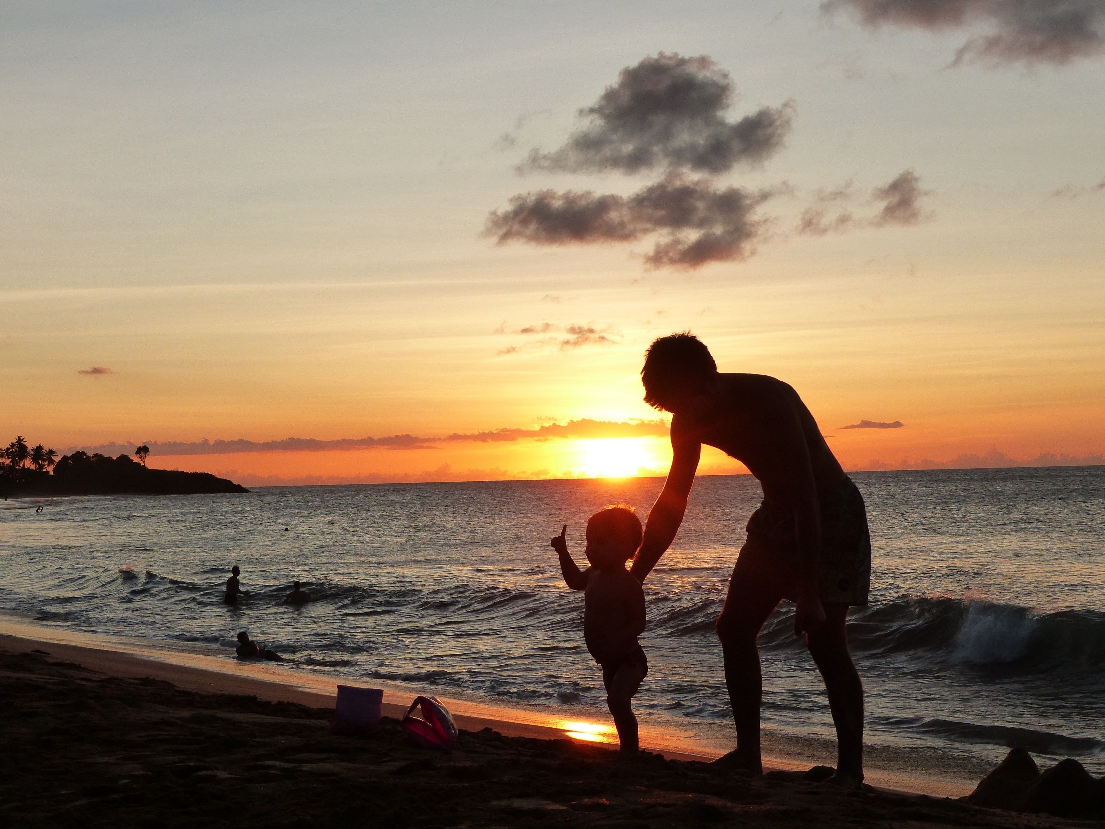 Silueta de una persona y un niño en la playa durante la puesta de sol.