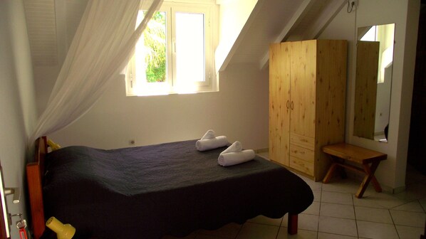 Un dormitorio con una cama, un armario de madera, un pequeño banco de madera y una ventana con cortinas.