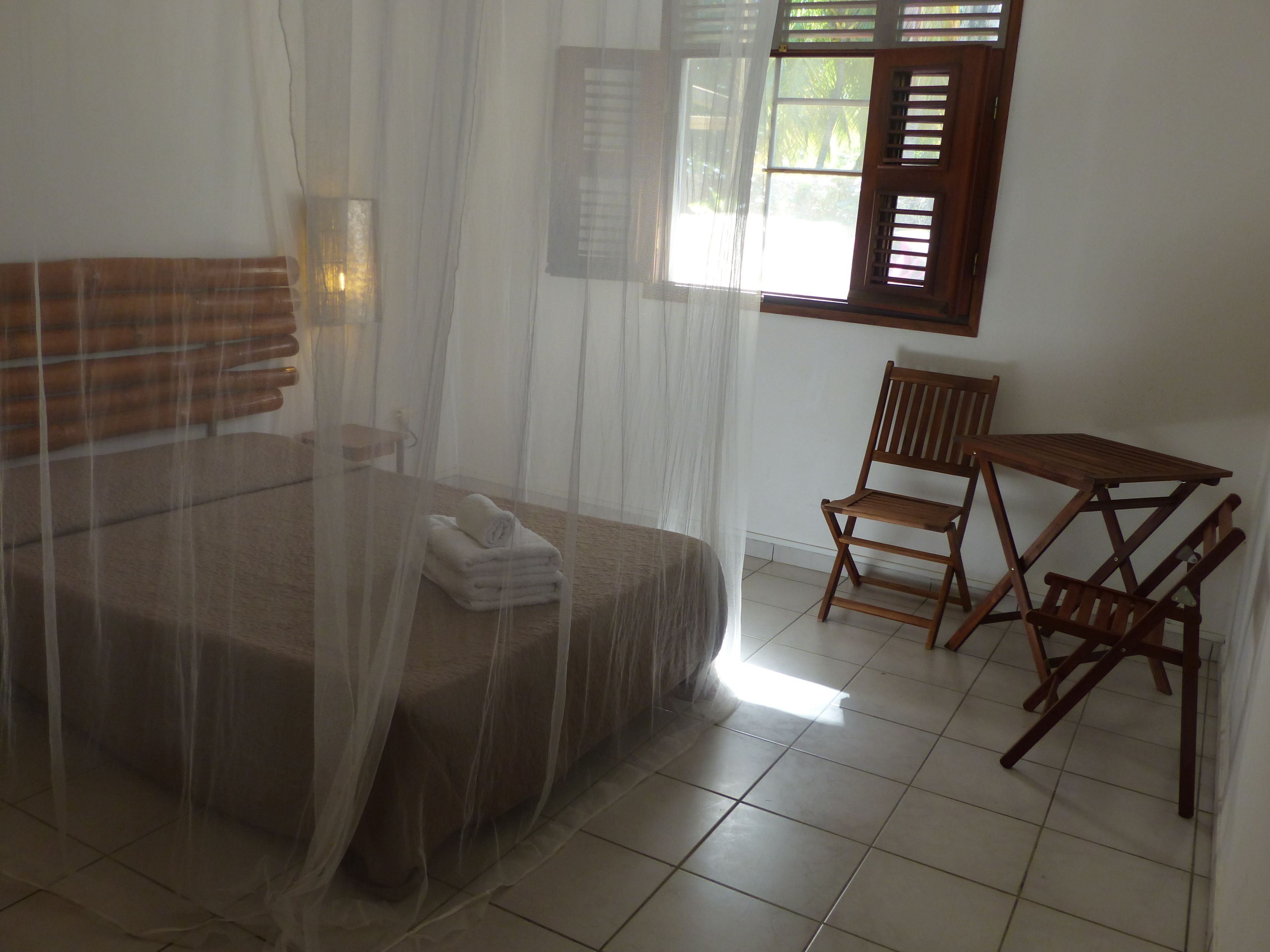 A room with a bed covered by a mosquito net, a small table, and a chair.